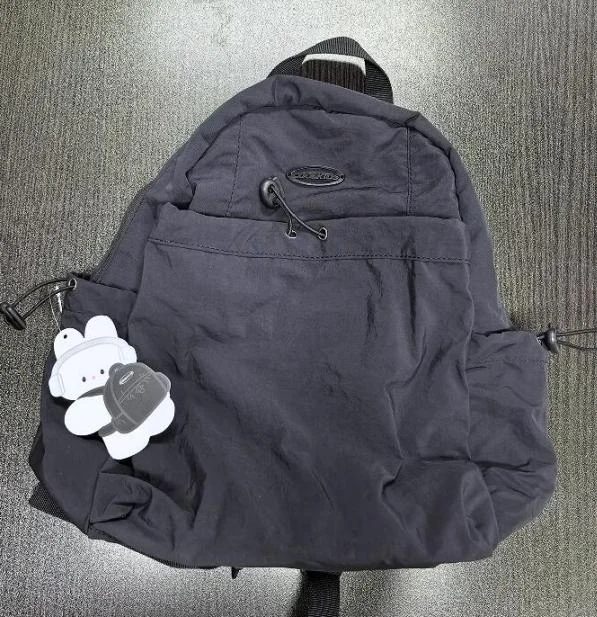 Dark backpack with front zipper pockets, top handle and a hanging product tag
